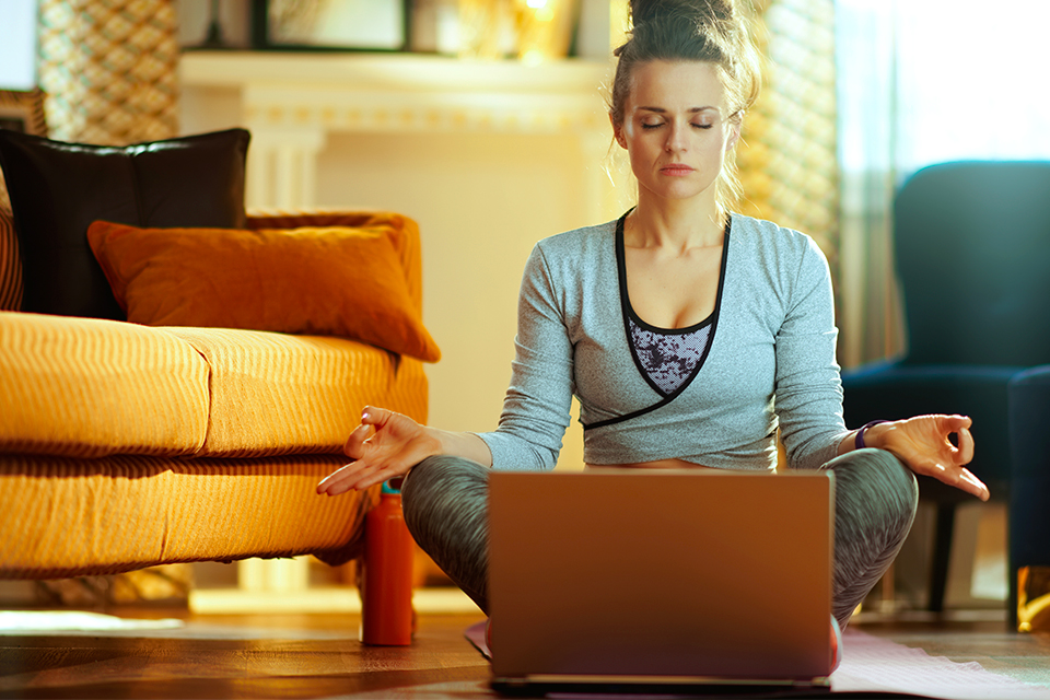 Frau sitzt auf dem Boden vor dem Laptop und meditiert.